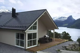 Hytte med Aerodek ståltakpanner som ser ut over en fjord. Takpannene er laget på en måte slik at de skal stå imot orkaner og nordisk hardt vær.