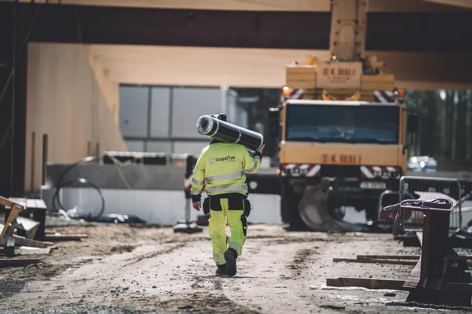 En taktekker fra IcopalTak går mot en arbeidsplass med en rull takbelegg på skulderen
