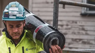 En taktekker med hjelm og en rull takbelegg på skulderen